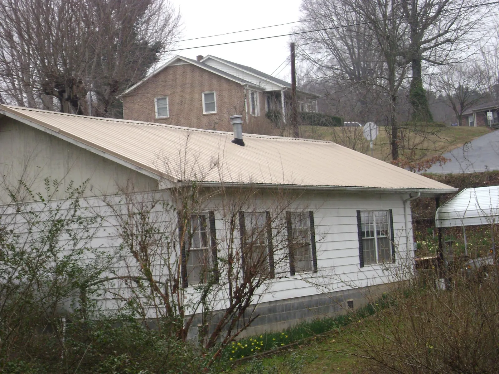 Tan metal roof on a white sided house set into a hillside — Commercial Roofing by Roofing Brothers in Oakley